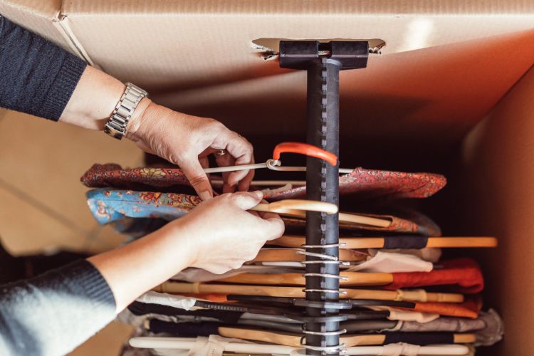 Una mujer colgando ropa en perchas dentro de una caja de cartón para textil